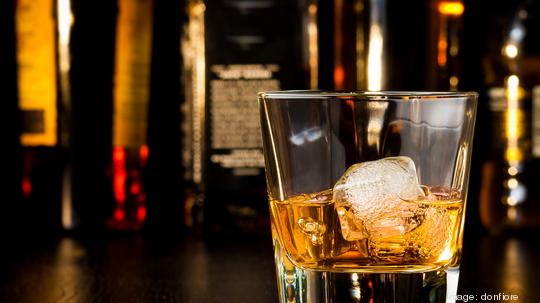 whiskey glass with ice in front of bottles