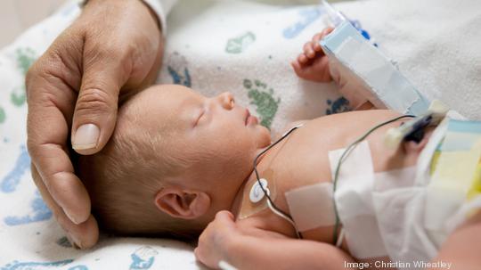 father touching head of a premature baby in incubator