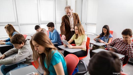 Teacher assisting high school student in a modern classroom.