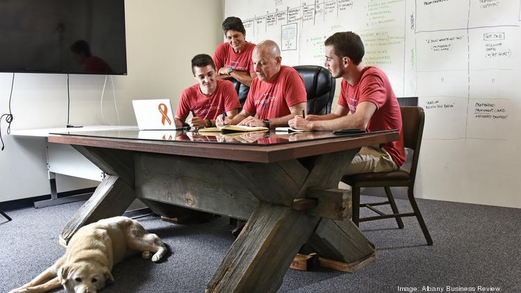 BuildPay staff Ross Wightman, product and business development, seated, left, with CEO Steven Wightman, Chartt Miller, marketing intern, and standing, Suzanne Wightman, administrative assistant. At the foot of the table is the family dog, Emma.