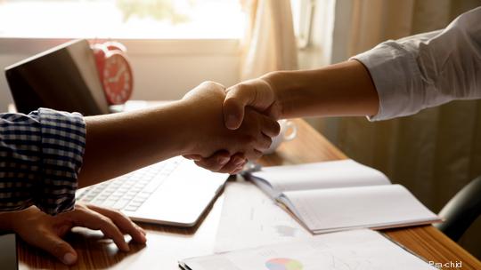 Two people shaking hands over the desk during meeting