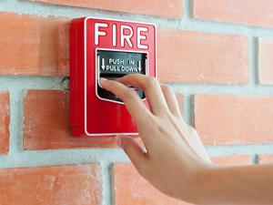 Hand pulling down fire alarm on brick wall