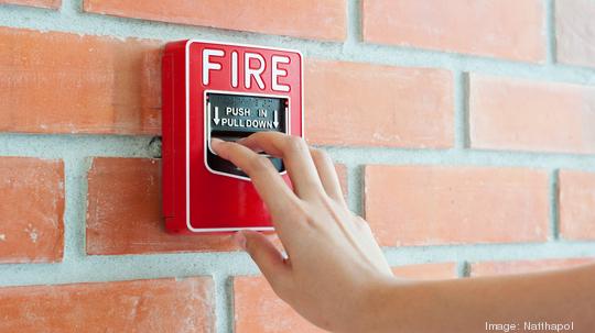 Hand pulling down fire alarm on brick wall