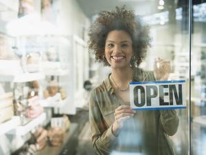 Black woman holding open sign in store window