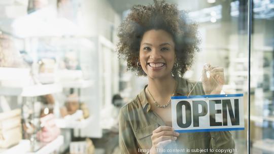 Black woman holding open sign in store window