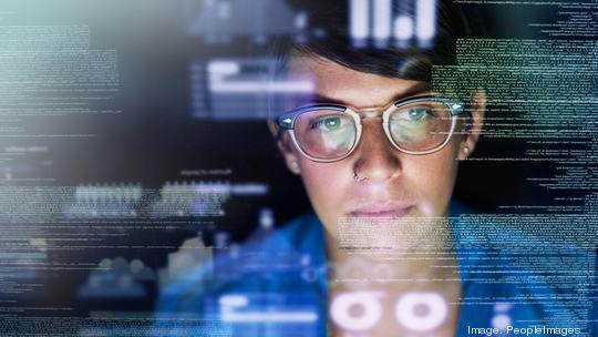 A young female computer programmer surveys data on a dark screen