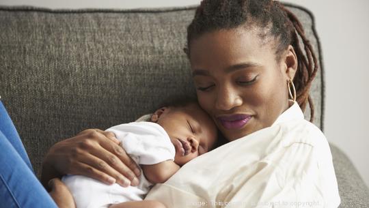 Black mother cuddling sleeping baby son on sofa