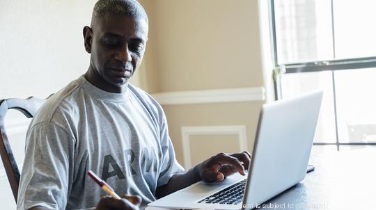 Black man using laptop and notebook at table