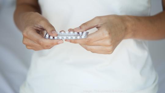 Woman holding birth control pills, mid section