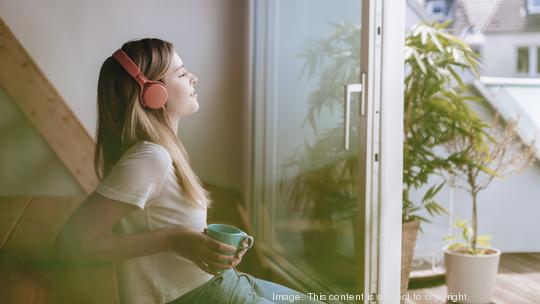 Young woman relaxing at home with a cup of tea, listening music