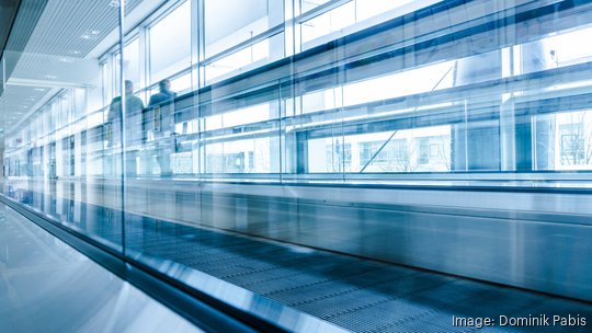 Businessmen moving on escalator in modern hall interior, office building