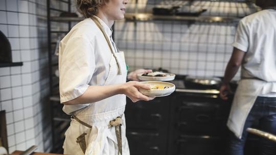 Midsection of waitress carrying food plates in kitchen at restaurant