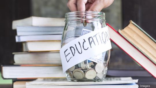 Coins and banknote in a glass jar placed on the textbook.