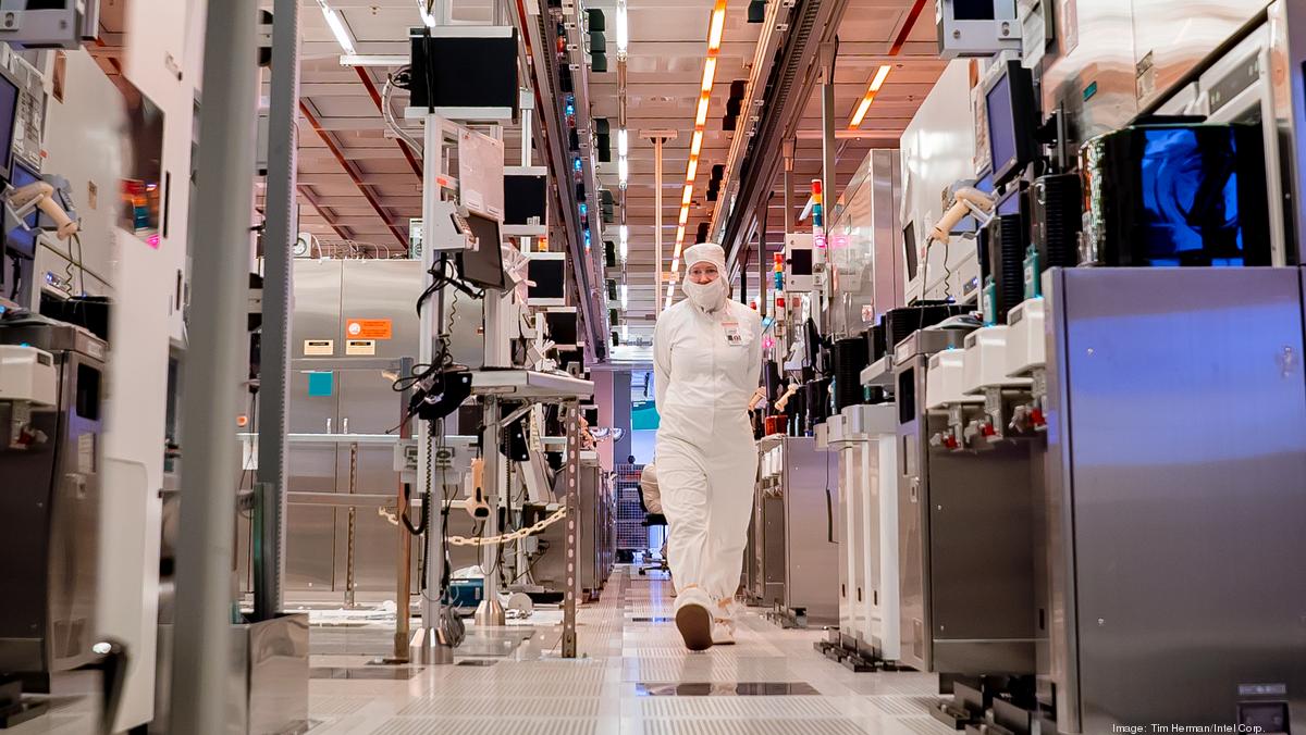  A photo of a worker in a white protective suit and hairnet walking in a semiconductor manufacturing cleanroom facility with the intent of illustrating the need for US government support for Intel's semiconductor manufacturing.