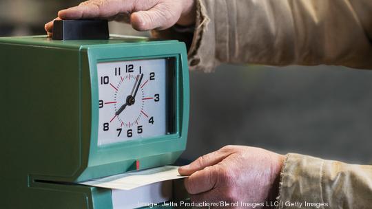 Caucasian worker punching time clock in warehouse Getty