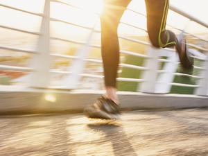 Runner couple running on sunny urban footbridge at sunrise