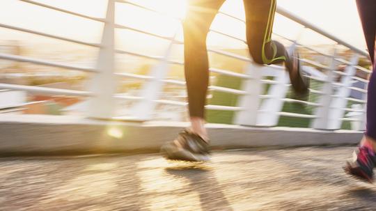 Runner couple running on sunny urban footbridge at sunrise