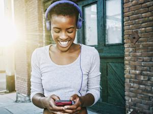 Smiling Black woman listening to cell phone with headphones in city