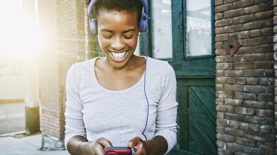 Smiling Black woman listening to cell phone with headphones in city