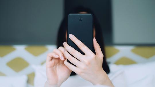 Portrait of woman using mobile phone while lying on bed