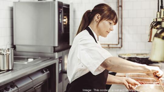 Side view of female chef preparing dish in commercial kitchen