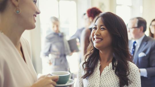 Smiling businesswomen drinking coffee and networking at business conference