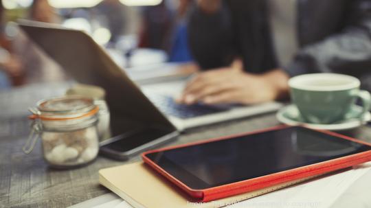 Creative businessman working at laptop behind digital tablet in cafe