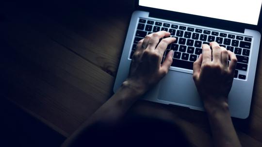 Close up of female hands working on laptop on table in the dark