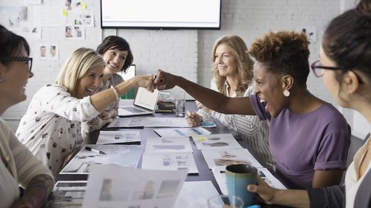 Female designers fist bumping in conference room meeting