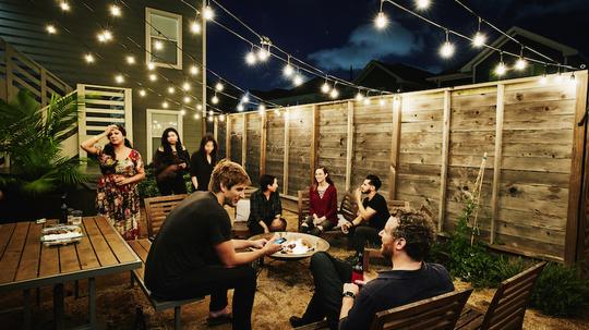 Friends sitting around fire during neighborhood backyard party on summer evening