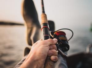 Low Section Of Man Fishing In Sea Against Sky During Sunset