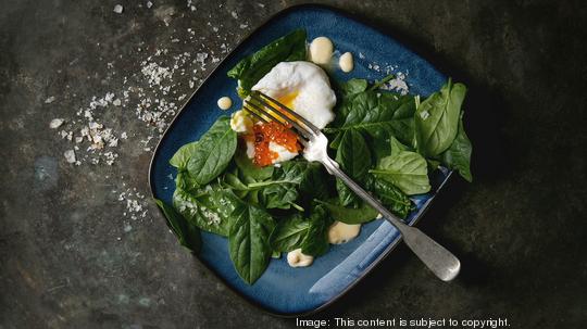 Poached egg on fresh spinach leaves with hollandaise sauce, red caviar served in blue square plate over old dark metal background. Top view, space. Vegetarian healthy eating