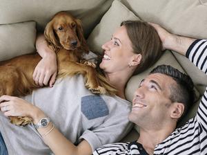 Smiling couple with dog lying on couch