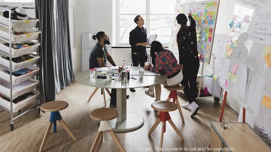 Businesswoman showing colleagues note on whiteboard during meeting in board room