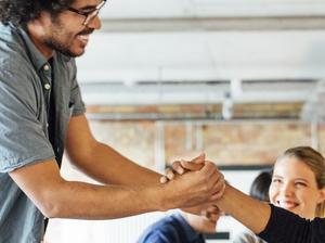 Smiling businessmen holding hands by colleagues at table