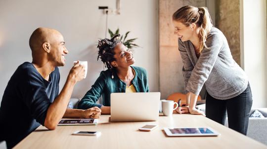 Business colleagues talking while using laptop at office