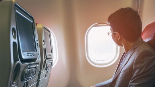 Young asian business man smiling and looking view at window in airplane