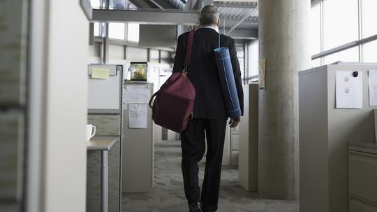 Businessman leaving office with gym bag and yoga mat