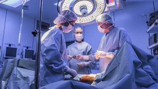 Surgeons operating on patient in operating theatre under lights