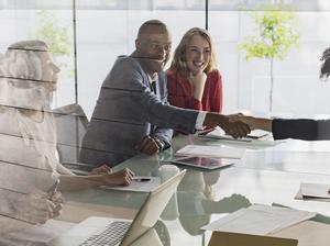 Businessman and businesswoman handshaking across conference table in meeting