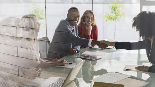 Businessman and businesswoman handshaking across conference table in meeting