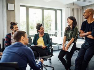 Colleagues looking at cheerful businesswoman in meeting