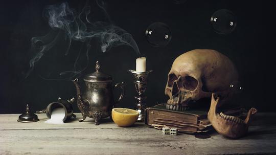 Close-Up Of Human Skull With Lemon And Candle On Table Against Black Background