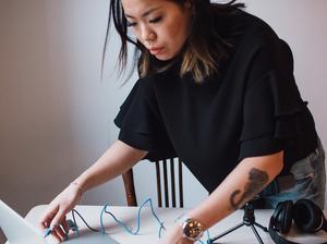 Female blogger using laptop standing by table with microphone at home