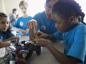 Male teacher helping pre-adolescent girls assembling robotics in classroom