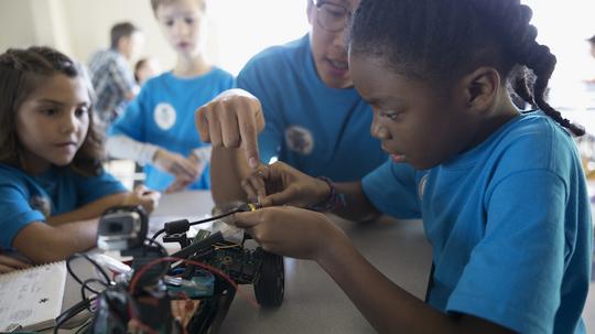 Male teacher helping pre-adolescent girls assembling robotics in classroom