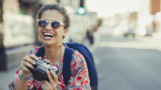 Portrait laughing, enthusiastic young female tourist in sunglasses photographing with camera on urban street