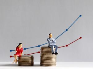 The concept of gender pay gap. A miniature man and a miniature woman sitting on top of a pile of coins at different heights in front of a bar graph.