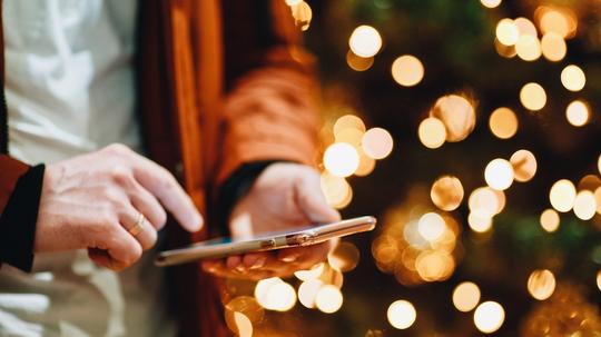 Midsection Of Man Using Smart Phone Against Illuminated Christmas Tree