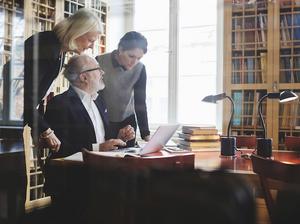 Senior lawyer discussing with female coworkers at table seen through glass in library